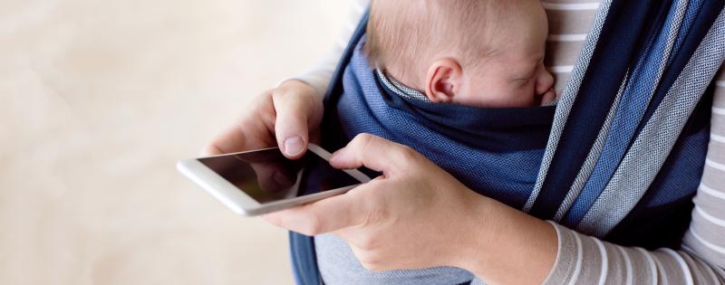 "Technoferenz" Eine Mutter hat ihr schlafendes Baby in einem Tragetuch und bedient gleichzeitig ihr Smartphone