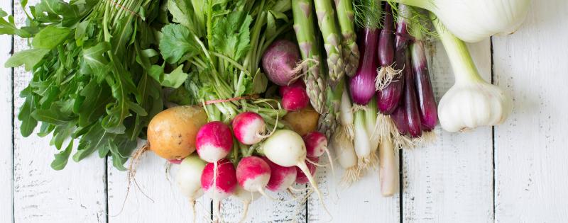 Verschiedene Gemüsesorten liegen auf einem Tisch: Rucola, Radieschen, Kartoffeln, Lauchzwiebeln, Spargel, Knoblauch, Fenchel.