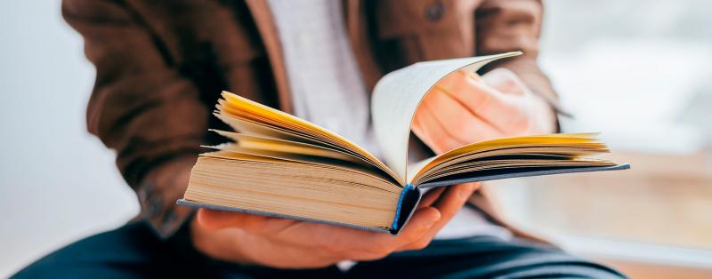 „HEAL“-Projekt will Lese- und Schreibkompetenz stärken Erwachsene Person blättert in einem Buch