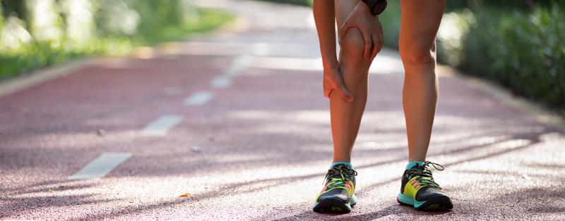 Beine eines Sportlers in kurzen Hosen, die Hände fassen an Knie und Wade