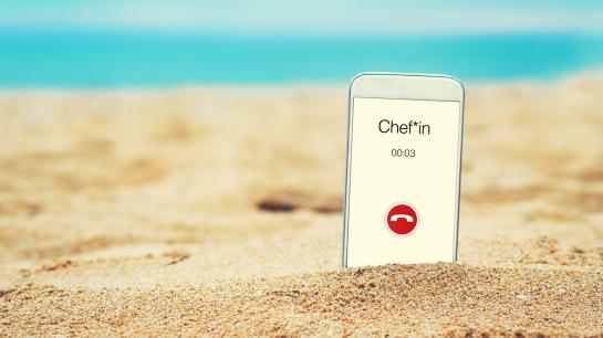 Handy steckt im Sand und auf dem Display erscheint "Chef"